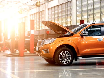 Ein orangefarbenes SUV steht in einer gut beleuchteten Auto-Werkstatt bei Autoankauf Viersen, dessen Motorhaube offen ist und den Motor zeigt.